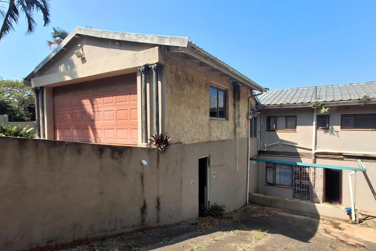 Rear view of the property showing a garage structure, concrete driveway, and multi-level exterior walls with visible signs of weathering and maintenance requirements.
