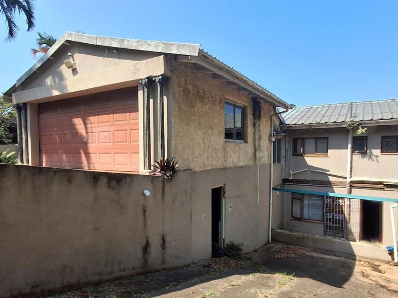 Rear view of the property showing a garage structure, concrete driveway, and multi-level exterior walls with visible signs of weathering and maintenance requirements.