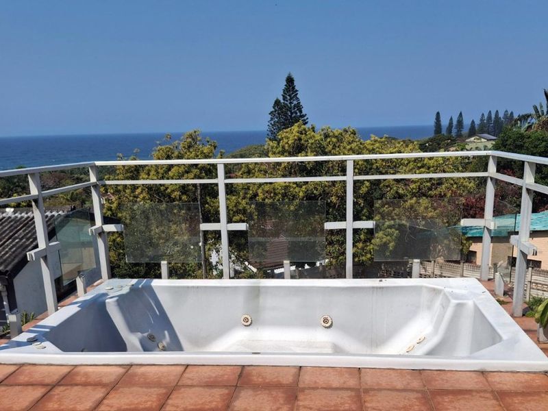 Outdoor balcony featuring a built-in jacuzzi, tiled flooring, and metal railings with glass panels, offering scenic ocean views.