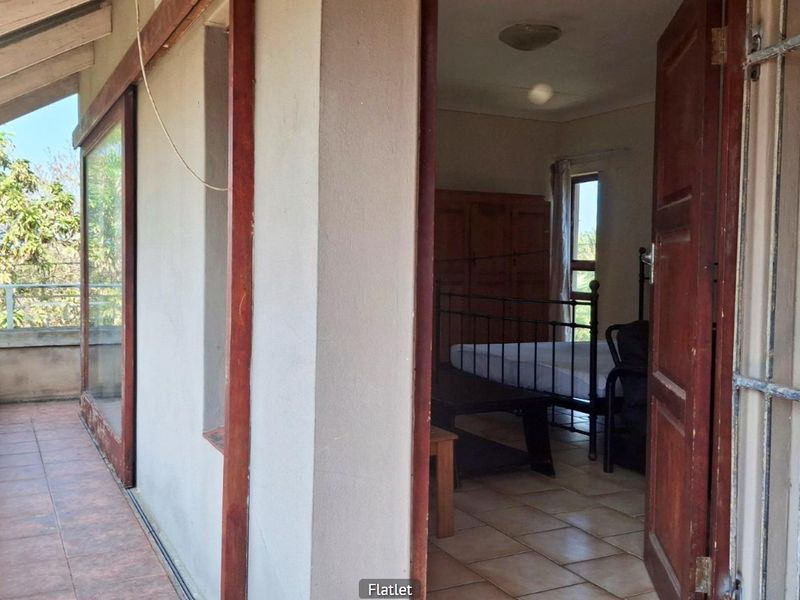 A covered balcony area with tiled flooring and security features, providing access to an interior bedroom space.
