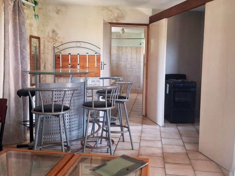 Open plan living area featuring tiled flooring and a built-in bar, requiring significant cosmetic repairs and wall restoration.