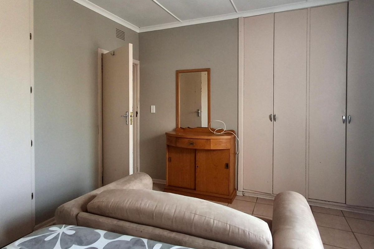 A bedroom featuring built-in cupboards, tiled flooring, and neutral wall finishes, offering a functional space with potential for modern updates.