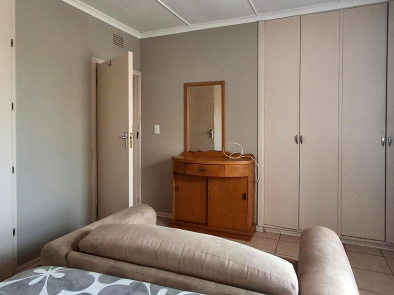 A bedroom featuring built-in cupboards, tiled flooring, and neutral wall finishes, offering a functional space with potential for modern updates.