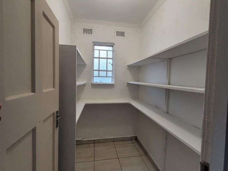 A functional scullery or pantry area featuring built-in shelving, tiled flooring, and a small window for natural light.