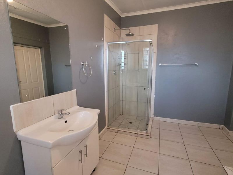 A functional bathroom featuring a vanity cabinet with basin, a glass-enclosed shower, and tiled flooring, presenting a clean but dated aesthetic.