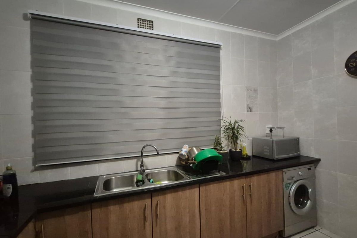 A functional scullery area featuring a double bowl sink, granite countertops, wood-finish cabinetry, and space for a washing machine.