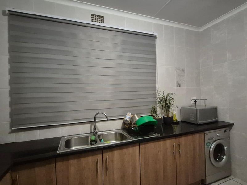 A functional scullery area featuring a double bowl sink, granite countertops, wood-finish cabinetry, and space for a washing machine.
