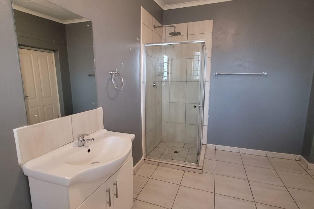 A functional bathroom featuring a vanity cabinet with basin, a glass-enclosed shower, and tiled flooring, presenting a clean but dated aesthetic.