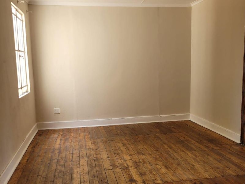 An empty bedroom featuring original timber flooring, neutral wall finishes, and a single window, offering a blank canvas for renovation or interior design.