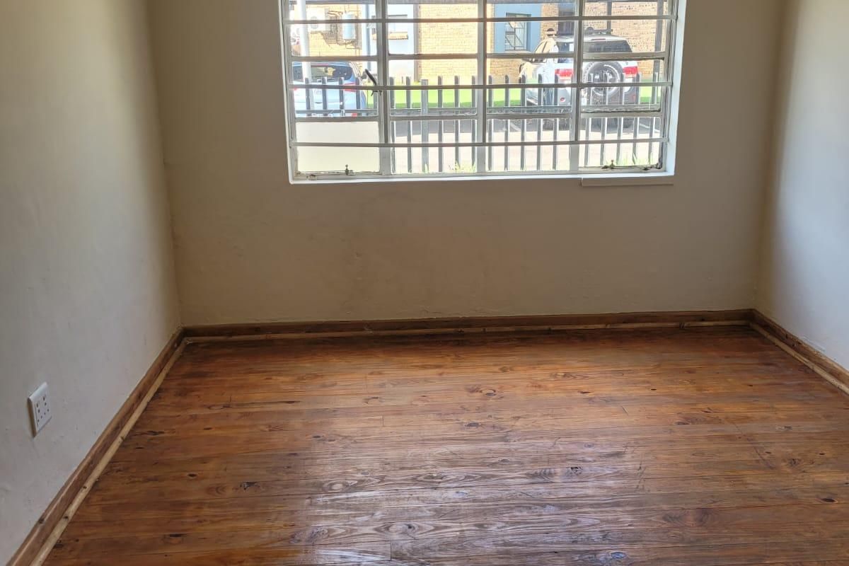 An empty bedroom featuring polished timber flooring, security bars on the window, and neutral wall finishes.