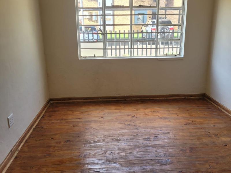 An empty bedroom featuring polished timber flooring, security bars on the window, and neutral wall finishes.