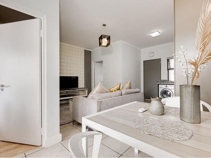 An open-plan living and dining area featuring a mix of tiled and laminate flooring, a textured feature wall, and modern lighting fixtures.