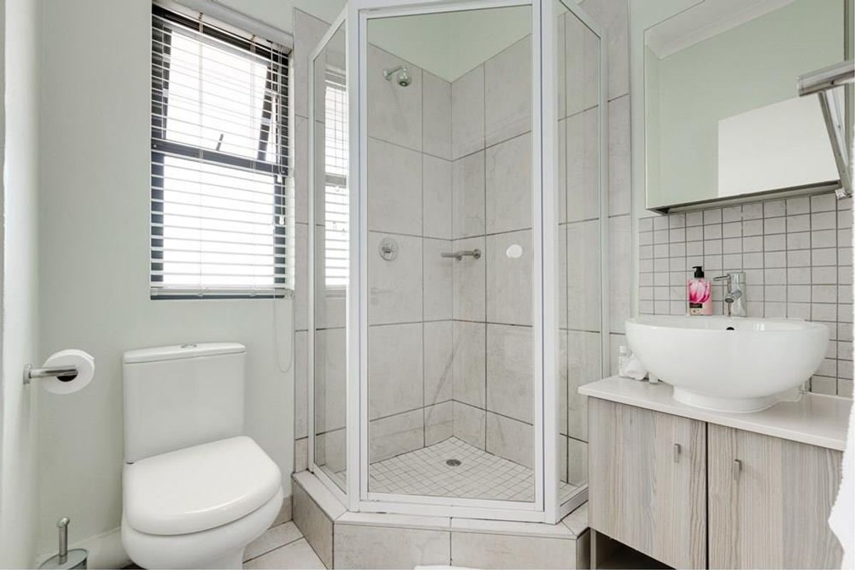 A clean and functional bathroom featuring a corner shower enclosure, a modern vessel sink with vanity storage, and a toilet.