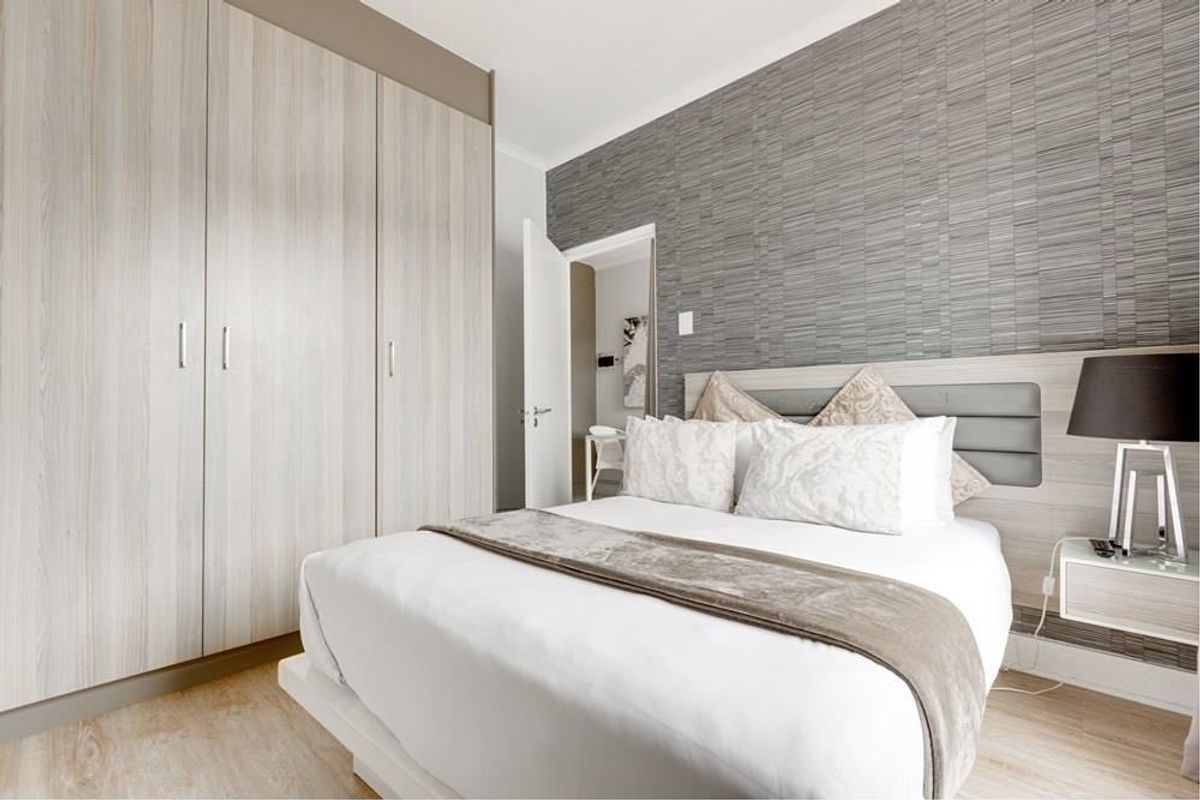 A well-maintained bedroom featuring modern built-in cupboards, a textured feature wall, and light-toned laminate flooring.