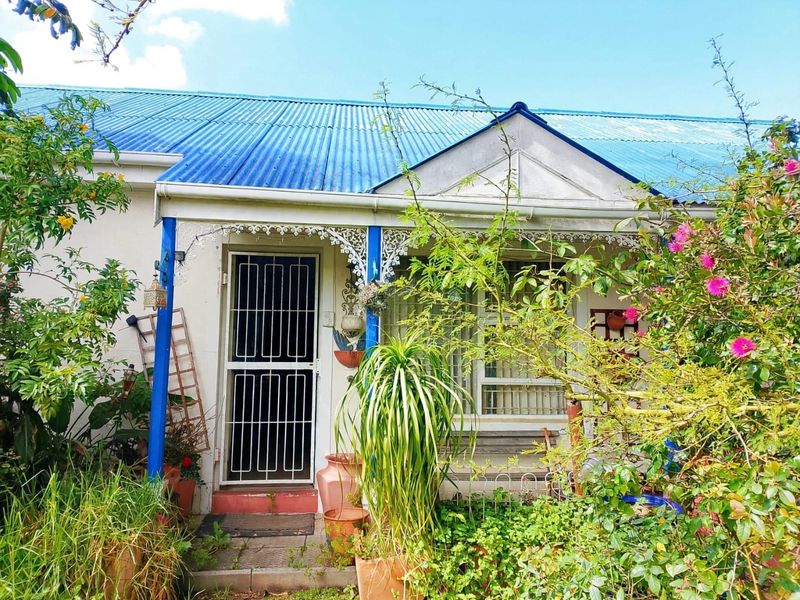 Front facade of a cottage-style home featuring a blue corrugated metal roof, a covered porch with decorative fretwork, and a security gate entrance.