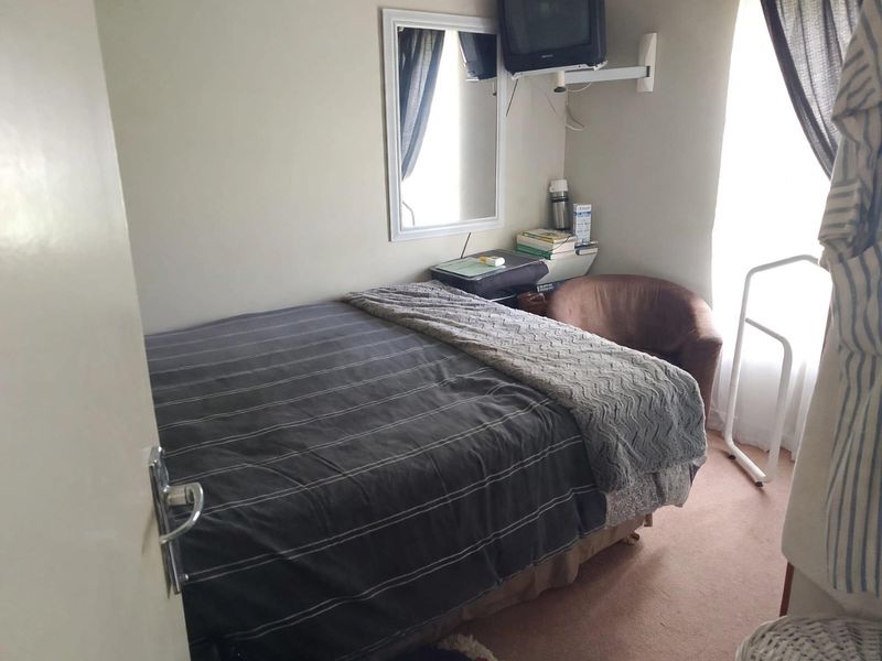 A compact bedroom featuring neutral wall finishes, a window for natural light, and a wall-mounted television bracket.