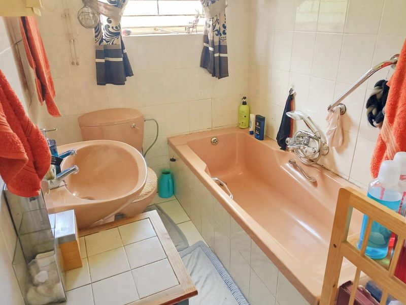 A functional bathroom featuring a vintage peach-colored bathtub, matching pedestal basin, and toilet, complemented by tiled wall finishes.
