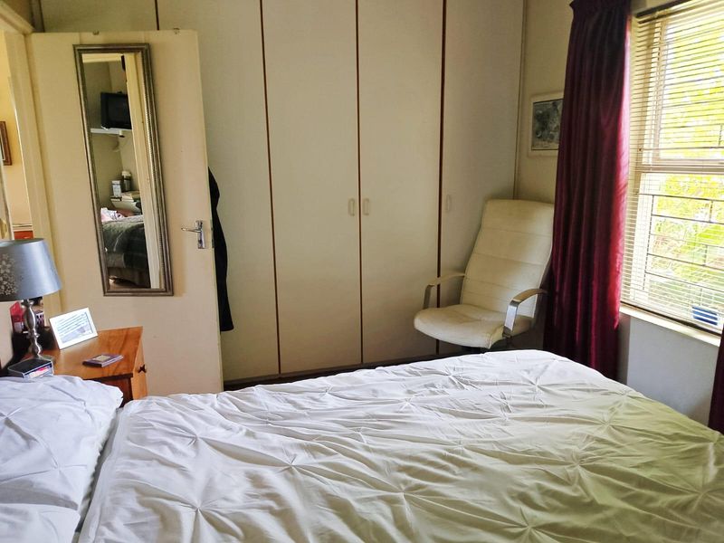 A functional bedroom featuring built-in cupboards and a window with security bars, offering a practical and comfortable living space.