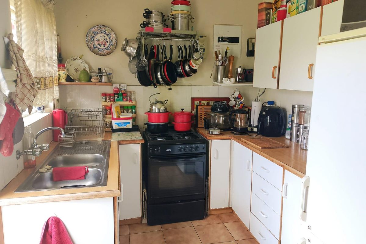A compact kitchen featuring a freestanding gas stove, double bowl stainless steel sink, laminate countertops, and ample wall-mounted cabinetry with tiled flooring.