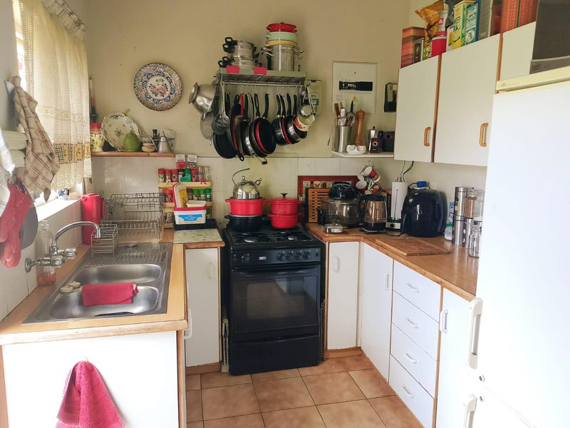 A compact kitchen featuring a freestanding gas stove, double bowl stainless steel sink, laminate countertops, and ample wall-mounted cabinetry with tiled flooring.
