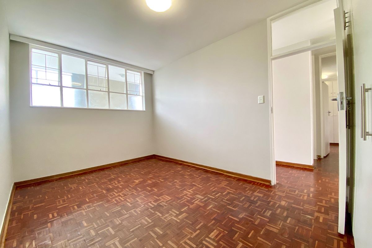 A bright, empty bedroom featuring classic parquet flooring, a large multi-pane window, and neutral walls, offering a clean canvas for personalization.