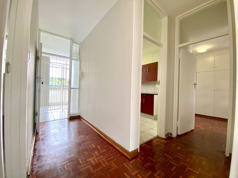 A bright, empty hallway featuring classic parquet flooring, built-in storage cupboards, and direct access to the kitchen and entrance area.