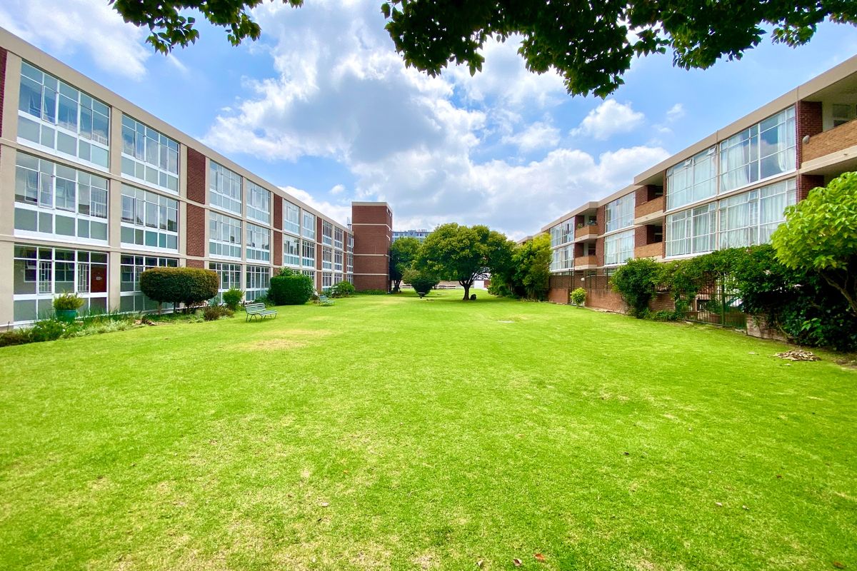 A well-maintained communal garden area situated between two apartment blocks, featuring expansive lawns and mature trees.
