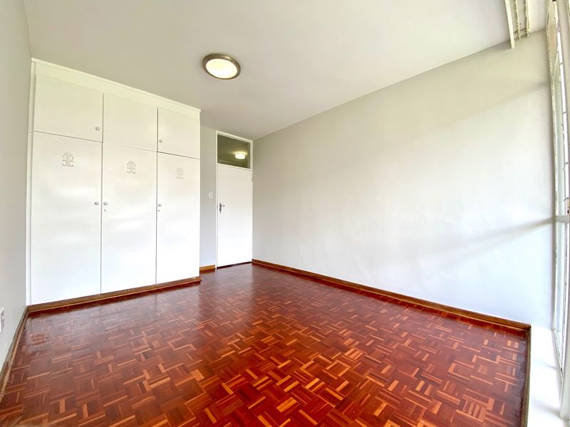 A bright, empty bedroom featuring classic parquet flooring and ample built-in cupboard storage, offering a clean and neutral space ready for personalization.