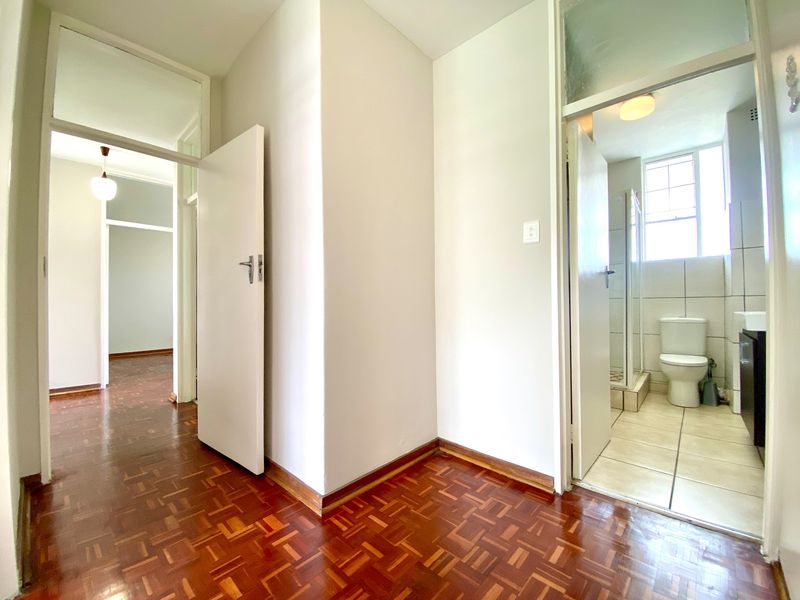 A bright hallway featuring classic parquet flooring, connecting to a bathroom and adjacent living spaces with traditional transom windows above the doorways.