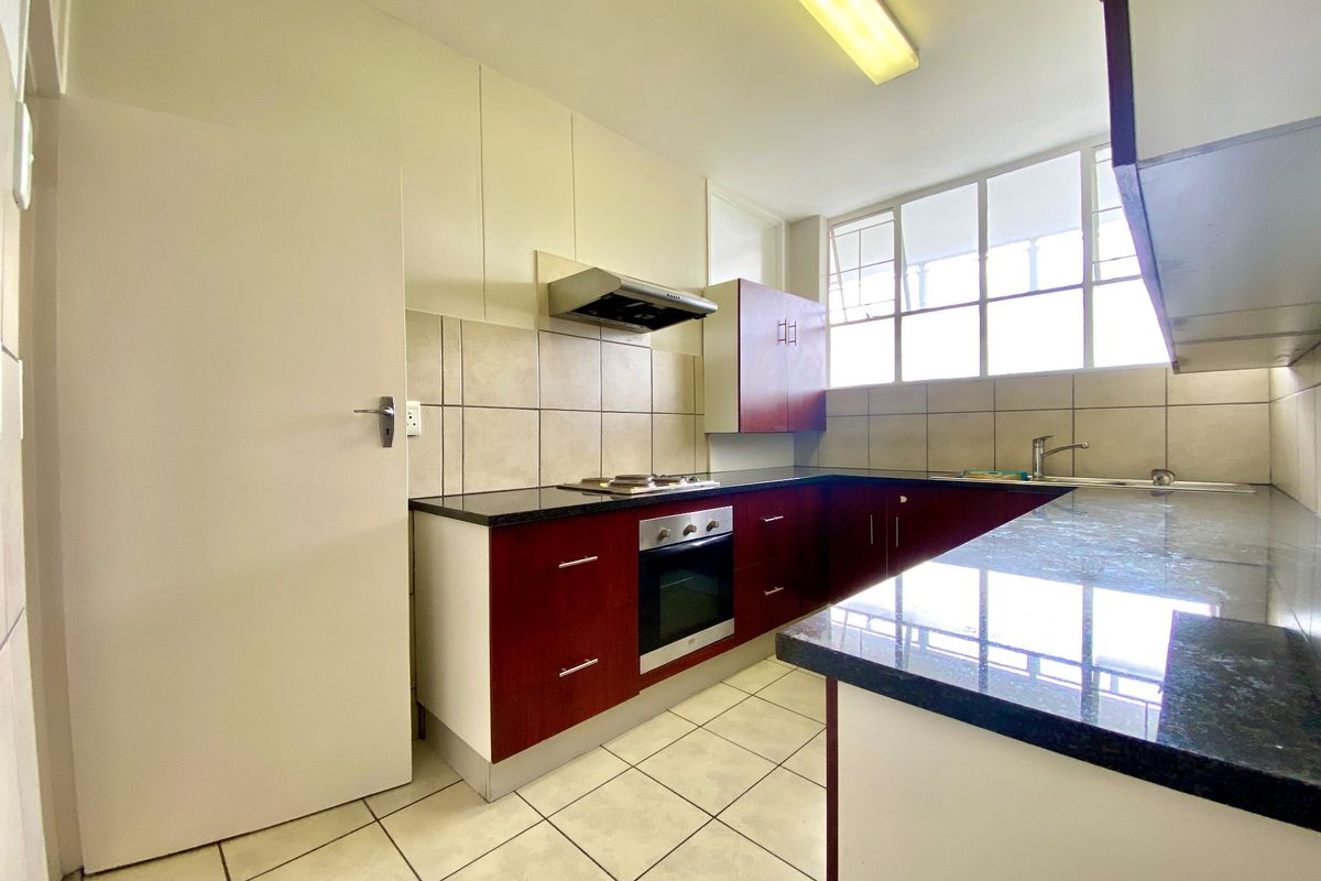 A functional kitchen featuring dark wood cabinetry, granite countertops, built-in oven, gas hob, and tiled flooring with ample natural light.