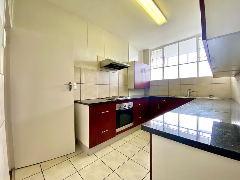 A functional kitchen featuring dark wood cabinetry, granite countertops, built-in oven, gas hob, and tiled flooring with ample natural light.