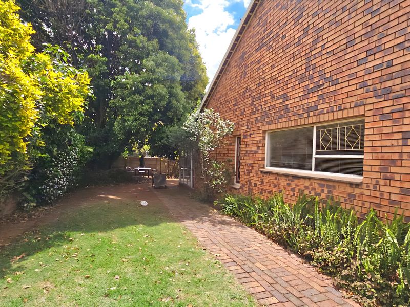 A view of the rear exterior of the house featuring a brick facade, a paved walkway, and a landscaped garden area.