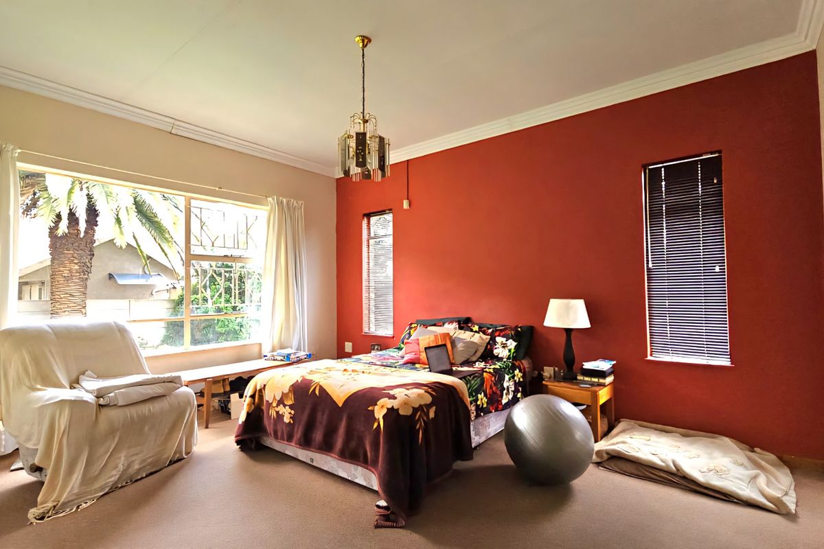 A spacious bedroom featuring large windows, neutral carpeting, and a bold accent wall, offering a bright and comfortable living space.