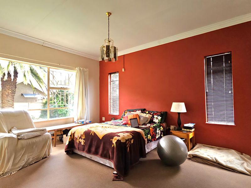 A spacious bedroom featuring large windows, neutral carpeting, and a bold accent wall, offering a bright and comfortable living space.