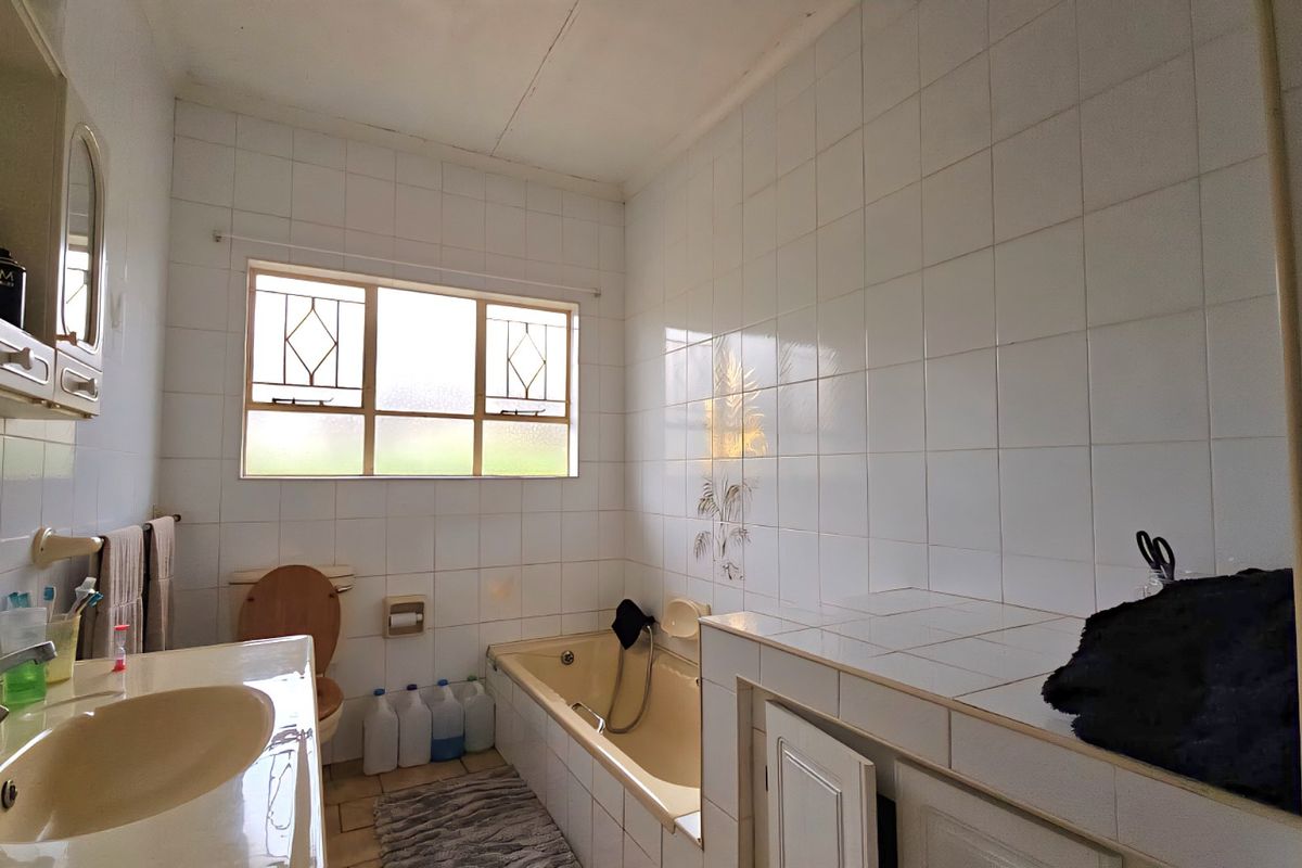 A functional bathroom featuring a built-in bathtub, tiled vanity countertop, and wall-mounted cabinetry, offering potential for a modern renovation.