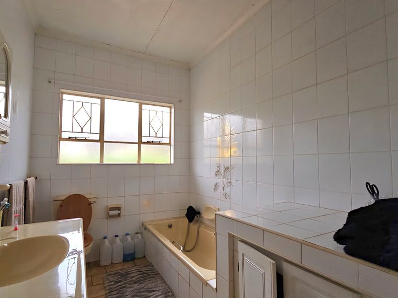A functional bathroom featuring a built-in bathtub, tiled vanity countertop, and wall-mounted cabinetry, offering potential for a modern renovation.