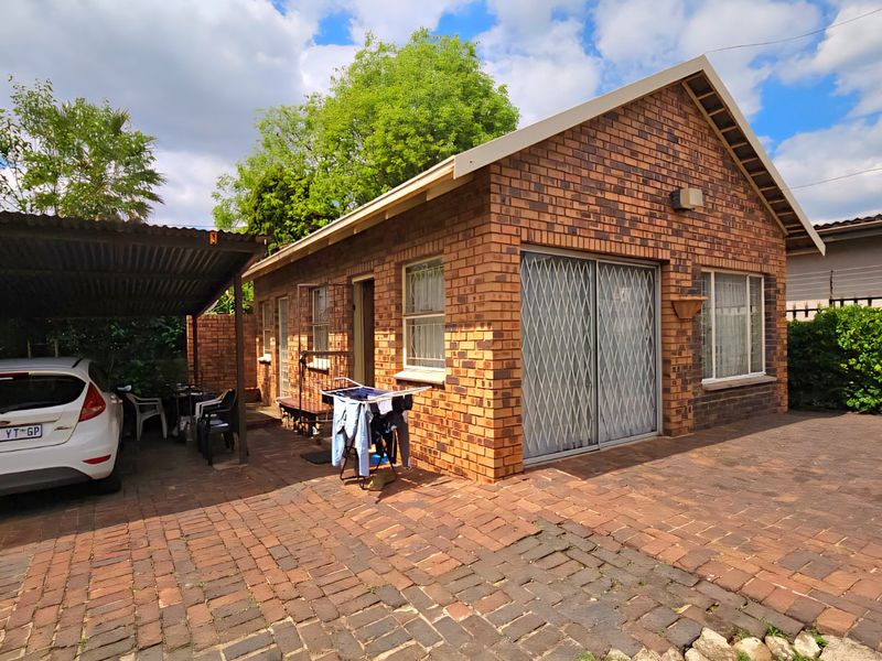 Exterior view of a face brick house featuring a paved driveway, attached carport, and secure metal entrance gates.