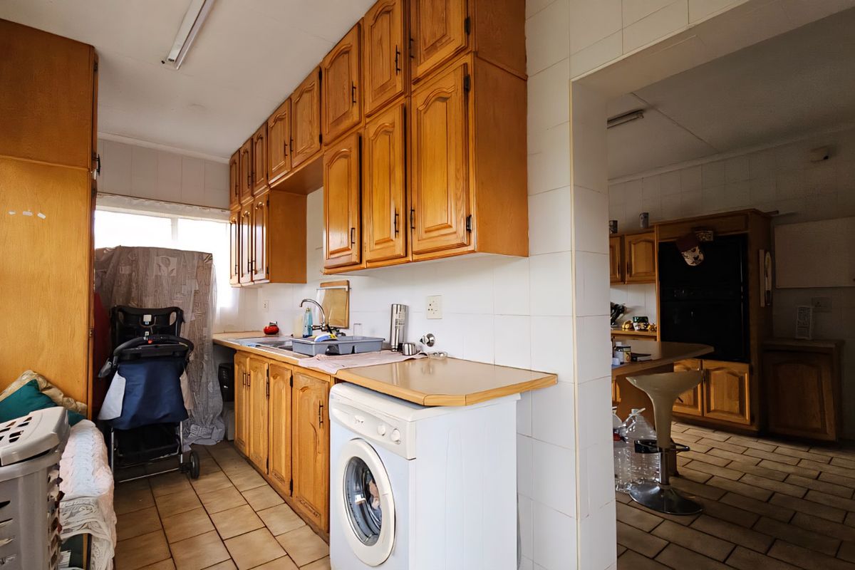 A dated kitchen featuring wooden cabinetry, tiled splashbacks, and tiled flooring, with an adjacent secondary prep or utility area visible through the doorway.