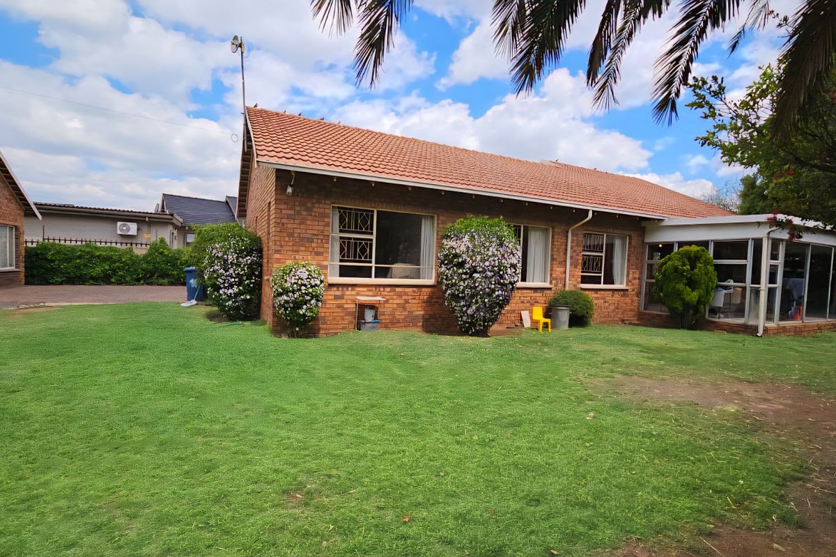 Rear view of a brick house featuring a tiled roof, security-barred windows, and an enclosed patio area overlooking a spacious garden.