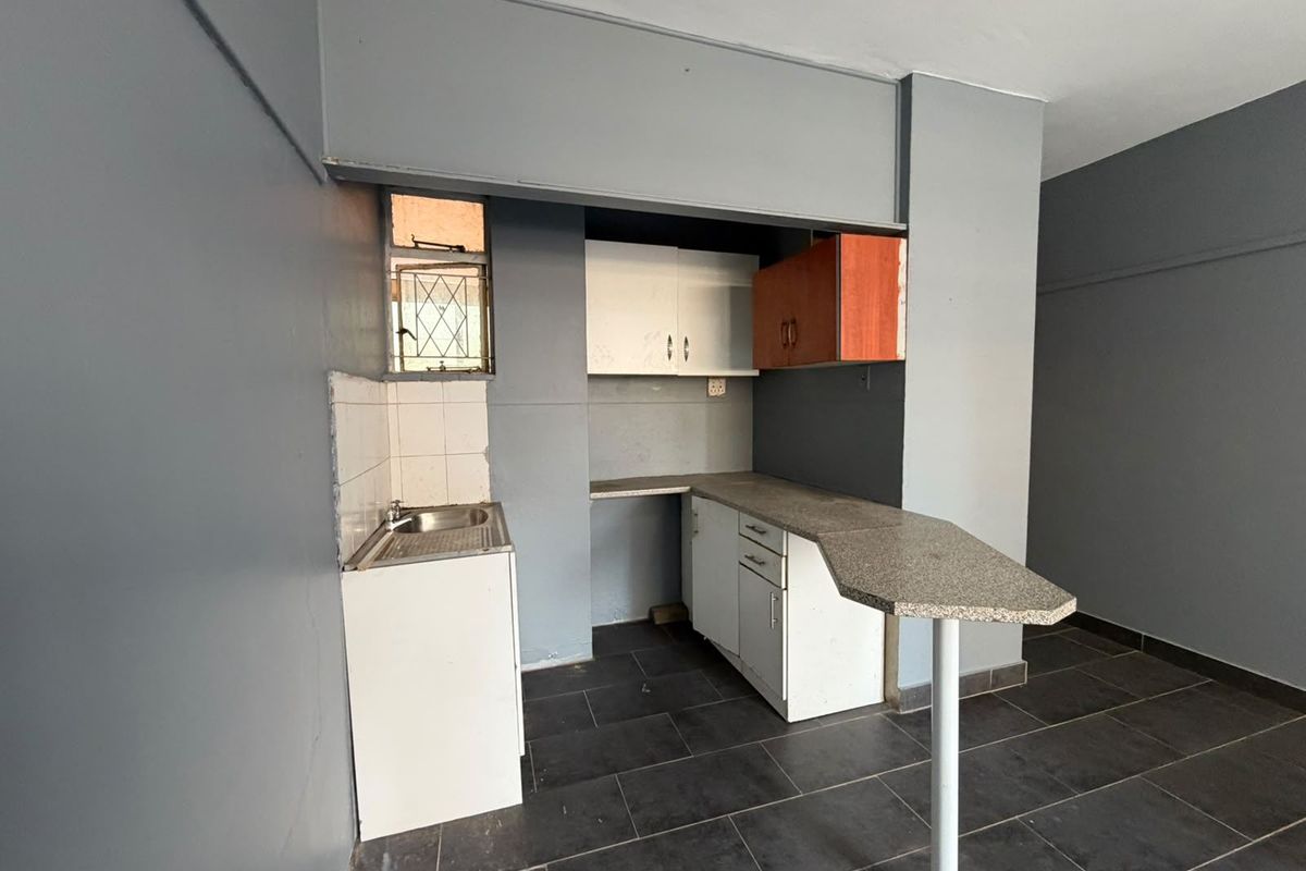 A compact, empty kitchen featuring dark tiled floors, basic cabinetry, a small sink, and an integrated breakfast bar, ready for renovation or modernization.