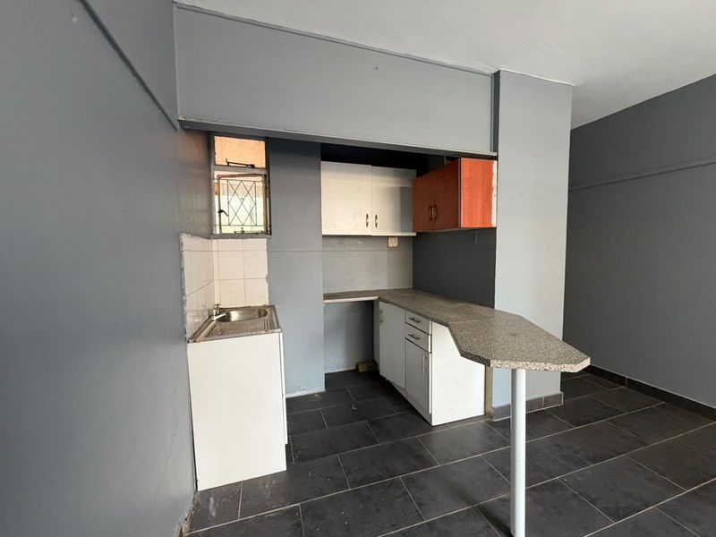 A compact, empty kitchen featuring dark tiled floors, basic cabinetry, a small sink, and an integrated breakfast bar, ready for renovation or modernization.