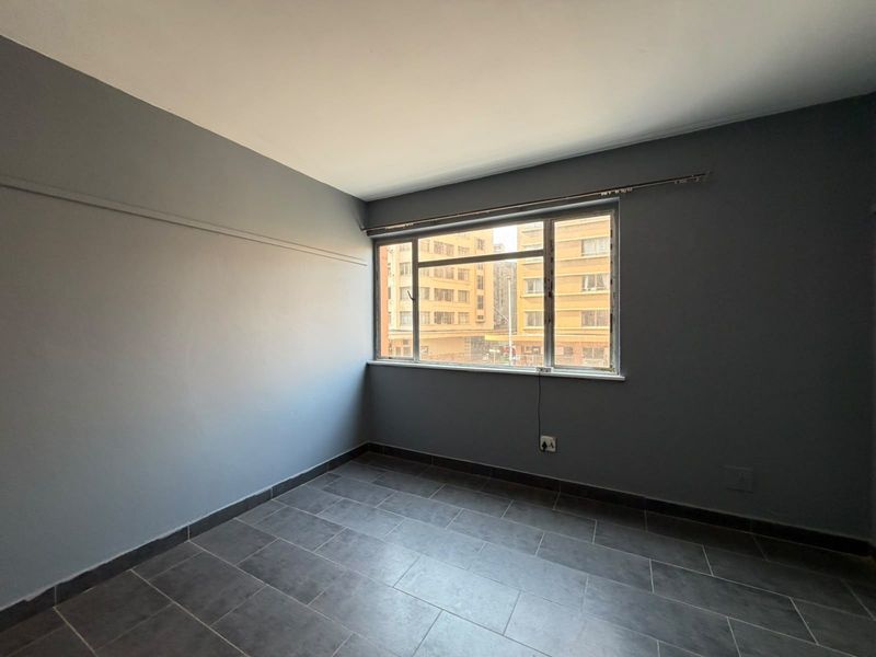 An empty bedroom featuring grey tiled flooring, dark grey painted walls, and a metal-framed window with an installed curtain rail.