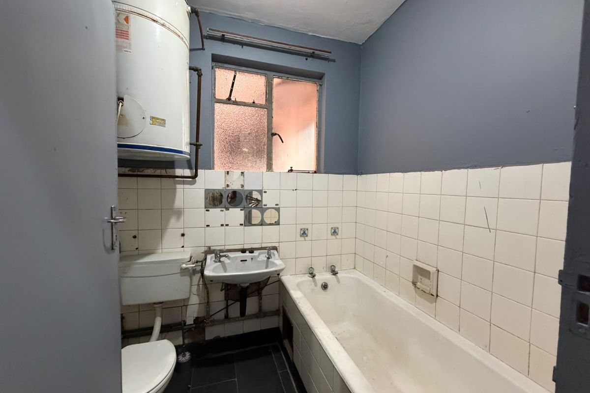 A dated bathroom featuring a bathtub, toilet, and washbasin, requiring significant renovation and modernization of fixtures and finishes.