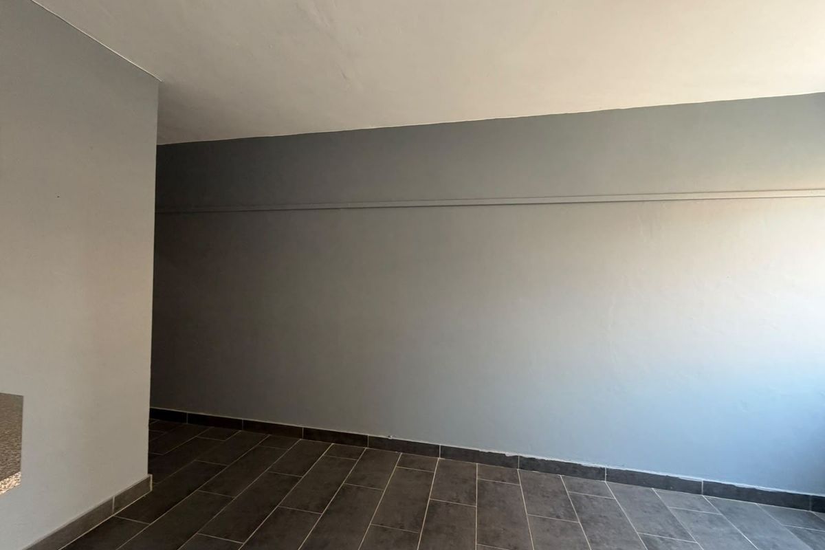 An empty living area featuring neutral grey walls and modern dark tiled flooring, providing a clean and versatile space ready for furnishing.