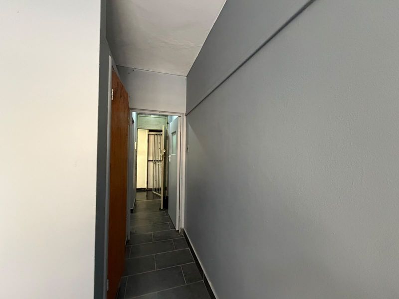 A narrow hallway featuring dark floor tiles and grey painted walls, leading to an interior doorway with a security gate.