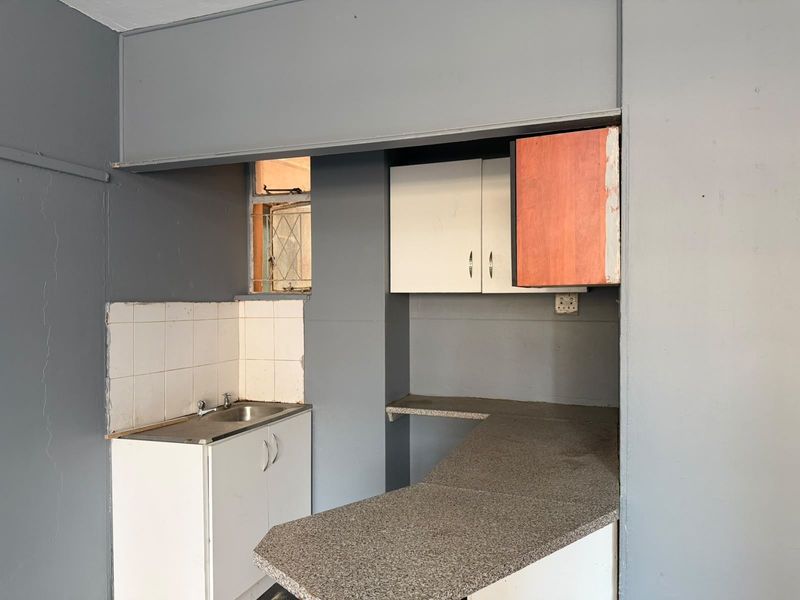 A compact kitchen area featuring a stainless steel sink, laminate countertops, and built-in cabinetry, currently in need of cosmetic updates and finishing.