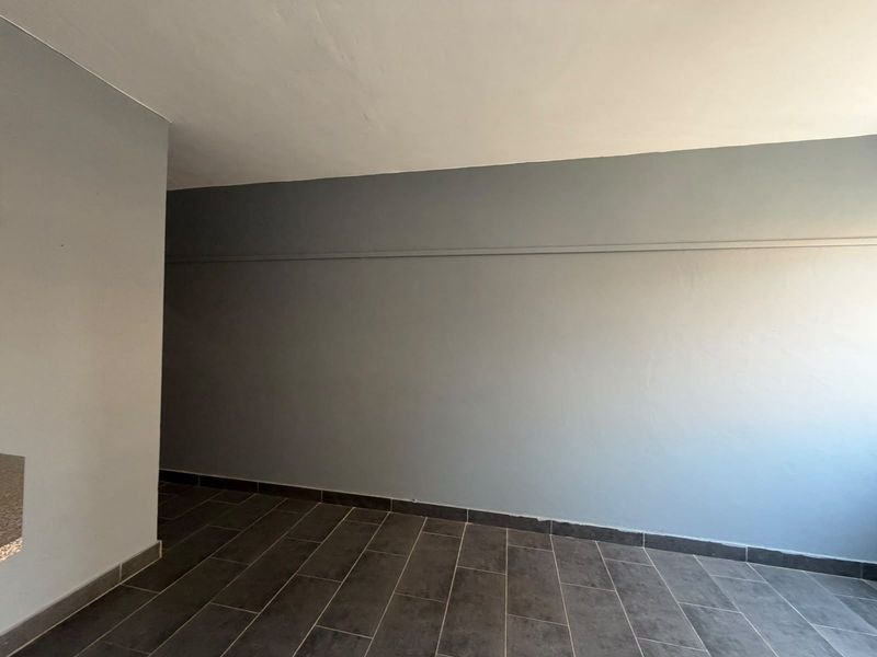 An empty living area featuring neutral grey walls and modern dark tiled flooring, providing a clean and versatile space ready for furnishing.