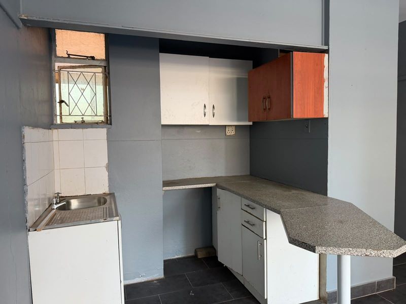 A compact kitchen area featuring built-in cabinetry, a stainless steel sink, and a breakfast bar, requiring cosmetic updates to modernize the space.