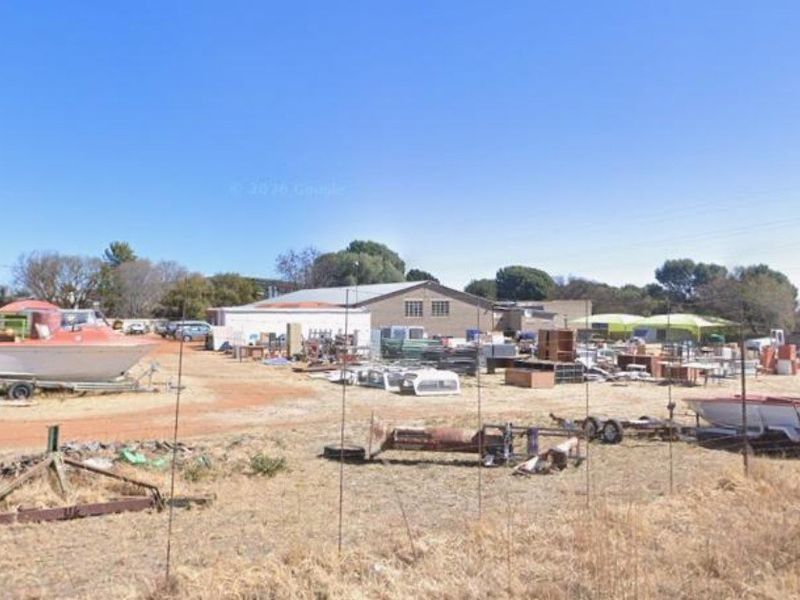 A wide view of a commercial property exterior featuring a large open yard area and a central industrial building structure.