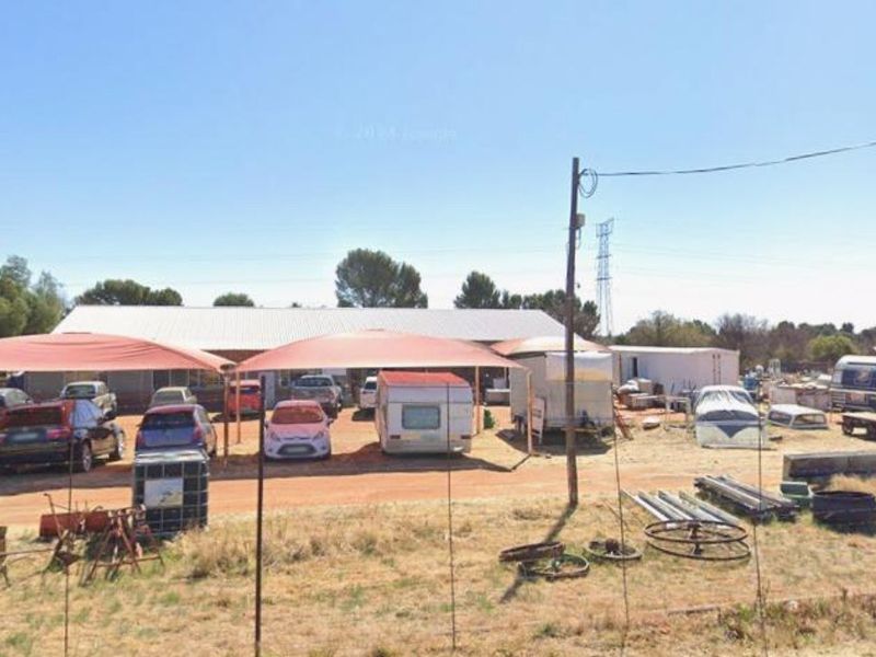 Commercial property exterior featuring a large signage pylon, shade structures, and an expansive unpaved yard area used for storage and parking.